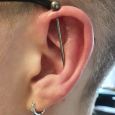A vertical industrial piercing on someone with glasses