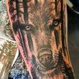 A wolf merging with the forest on a forearm