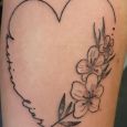 A minimalist tattoo of a heart with a message and flowers