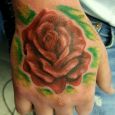 A red rose with a green background tattooed on the hand